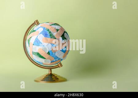 Round shaped globe of Planet Earth plastered with numerous medical band aids placed on light green background Stock Photo