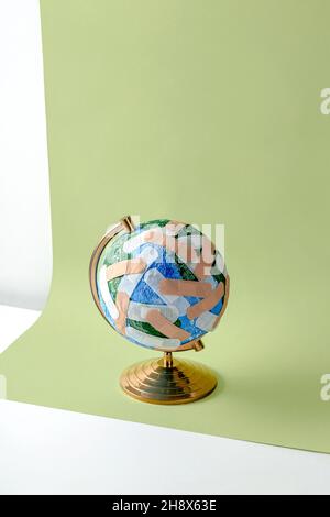 Round shaped globe of Planet Earth plastered with numerous medical band aids placed on light green background Stock Photo