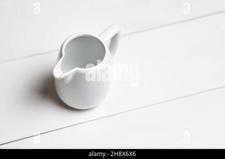 Empty milk jug on wooden background. Porcelain sauce boat, pitcher, creamer or ceramic gravy boat Stock Photo