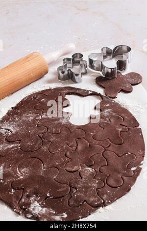 Rolled out chocolate gingerbread dough with cut out gingerbread man shapes with cookie cutter. Stock Photo