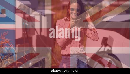 British flag over smiling young woman talking on mobile phone against charging electric car Stock Photo