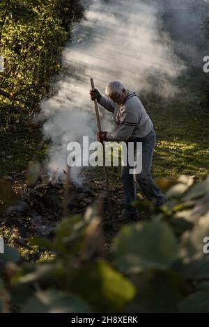 RAJHRAD, CZECH REPUBLIC - Oct 22, 2021: An old man burning leaves in the garden in autumn Stock Photo