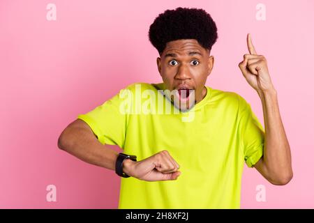 Portrait of attractive amazed guy pointing up looking at watch minute isolated over pink pastel color background Stock Photo