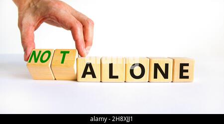 You are not alone symbol. Businessman turns wooden cubes and changes words alone to not alone. Beautiful white table white background, copy space. Bus Stock Photo