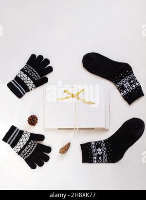 New year flatlay. Christmas black ornamental socks and gloves, blank white notebook with ribbon bow. Mockup template design. Winter decorations, pine Stock Photo