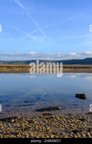 Reflections of vapour trails and clouds in the estuary at Red Warf Bay, Anglesey, North Wales, UK Stock Photo