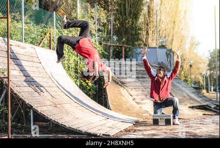 Urban athlete breakdancer performing somersault jump flip at skate park - Afroamerican guy watching friend acrobat dancing with extreme flipping move Stock Photo