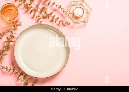 Christmas table setting with eucalyptus leaves and luxury metallic golden decorations at pink layout. Stock Photo