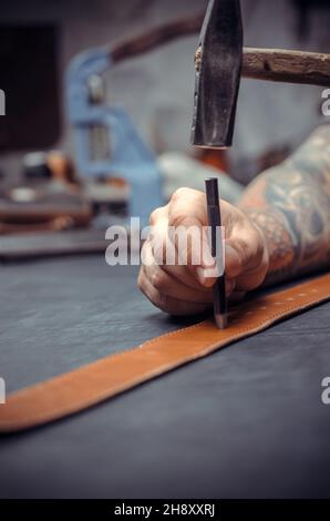 Handicraftsman performs leather working for a new product in leather shop Stock Photo