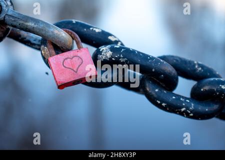 Red padlock with heart closed on black chain and unfocused background Stock Photo
