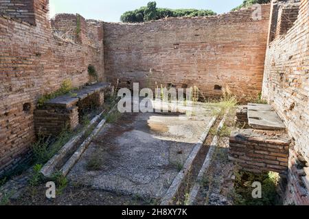 The well-preserved remains of an ancient Roman public bathroom with travertine seats and toilet drains, under the seats, the drains were constantly cl Stock Photo