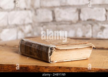An old book in a battered binding lies against a brick wall made of light brick. Stock Photo