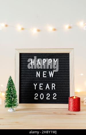 Happy new year 2022 written on black felt letter board and small Christmas tree and candle on wooden table Stock Photo