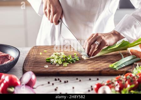 Chef finely chops spring onion on a wooden cutting board. Stock Photo