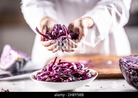 Thinly sliced raw red cabbage in hands and inside the bowl of a professional chef. Stock Photo