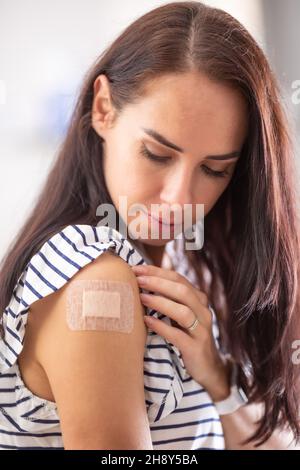 Vaccinated female looks at the plaster on her right shoulder. Stock Photo
