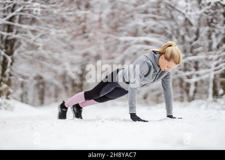 Sportswoman doing push ups on snowy path in nature at winter. Winter fitness, snowy weather, healthy life Stock Photo