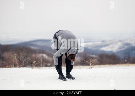 Sportsman in shape doing stretching exercises in nature on snowy winter day. Healthy habits, outdoor fitness, winter fitness Stock Photo