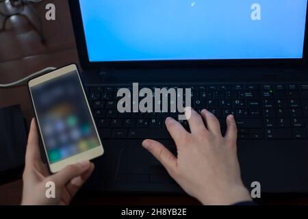 Woman's right hand on the laptop keyboard and holding mobile phone in the left hand Stock Photo