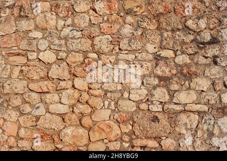 Rough reddish color stone bricks wall, sun shines on Stock Photo