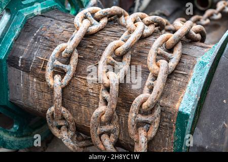 Rusty anchor chain around wooden coil Stock Photo