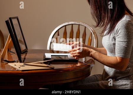 A young caucasian woman is placing a printed photograph into a picture frame with kickstand. There are other frames on the table. Tabletop picture fra Stock Photo