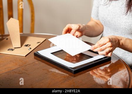 A young caucasian woman is placing a printed photograph into a picture frame with kickstand. There are other frames on the table. Tabletop picture fra Stock Photo