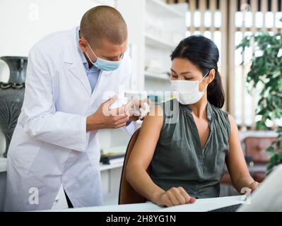 Doctor vaccinating asian businesswoman at work desk in office Stock Photo