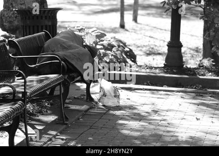 Grayscale shot of a homeless person sleeping on a bench in a park Stock Photo