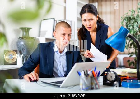 Upset office employe looking on laptop with disgruntled female manager Stock Photo