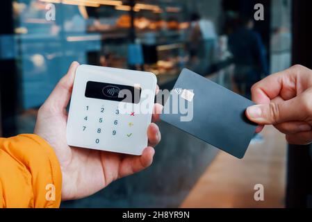 Crop faceless customer with credit card making contactless purchase on POS terminal in cafe in city Stock Photo