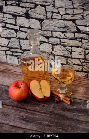 Apple calvados, spirits and ripe fruit stand on a wooden table against a stone wall. Vertical positioning. Stock Photo