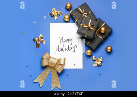 Greeting card with text HAPPY HOLIDAYS, Christmas decor and gift boxes on blue background Stock Photo