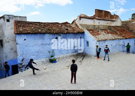 Moroccan boys playing football between the traditionally blue painted houses in the medina of Chefchaouen in the Rif mountains in northern Morocco. Stock Photo