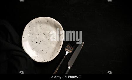 Minimal handmade ceramic plate with modern cutlery on a black table with copy space. top view Stock Photo