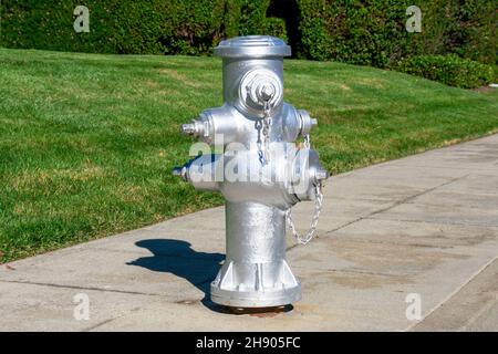 Chrome silver fire hydrant on sidewalk. Green grass and trees landscaping background. Stock Photo