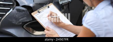 Woman insurance agent filling out paperwork near wrecked car closeup Stock Photo