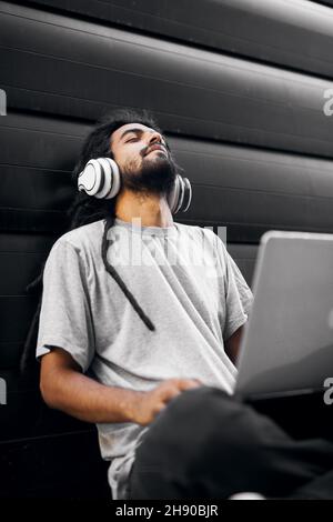 Casual indian hipster sitting on the street enjoying listening to music. Stock Photo