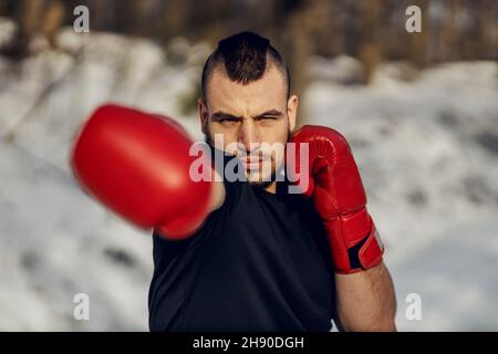 Strong muscular fighter with boxing gloves sparring in nature at snowy winter day. Boxing, winter fitness Stock Photo