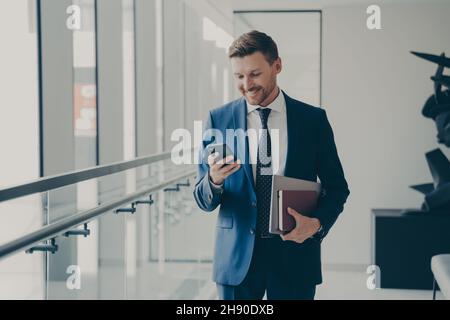 Happy handsome man ceo executive holding mobile phone and smiling during coffee break in office Stock Photo