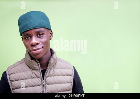 Positive black man in trendy clothes and cap looking at camera against green background in studio Stock Photo
