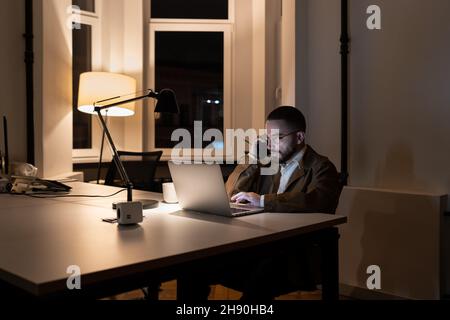 Young businessman, journalist or pr manager work at night on new project in empty coworking space Stock Photo