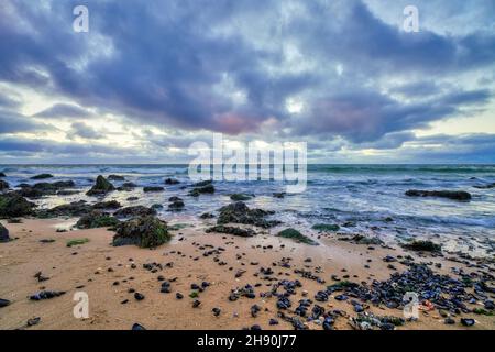 Landscape, seascape sunset on the coast of Huisduinen, the Netherlands. long exposer of waves, dramatic sky, detailed, seaweed, rocks. Stock Photo