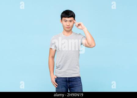 Young smart Asian man thinking with hand pointing on head in isolated light blue studio background Stock Photo