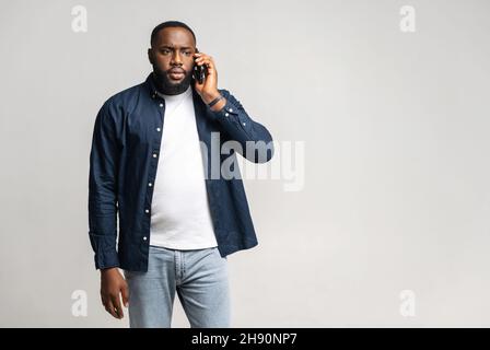Disappointed African-American man talking on the smartphone standing isolated on grey background, black guy has unpleasant phone conversation Stock Photo