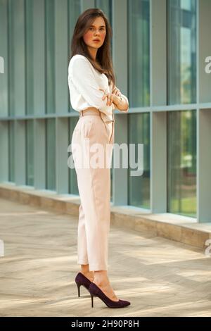 Full-length portrait young beautiful brunette woman in white blouse and pink  pants in office Stock Photo - Alamy