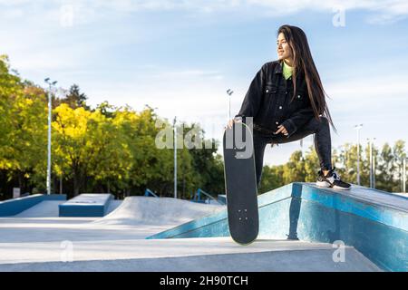 Stylish cool teen female skateboarder at skate park.