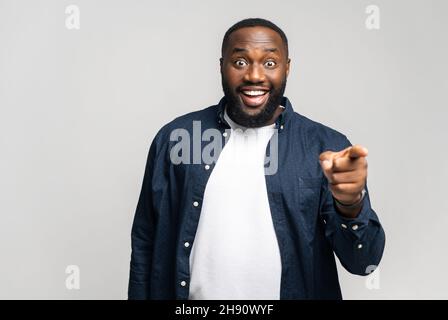 We need you. Happy African guy choosing you, pointing index finger at the camera with happy excited face, giving job opportunity or deal Stock Photo