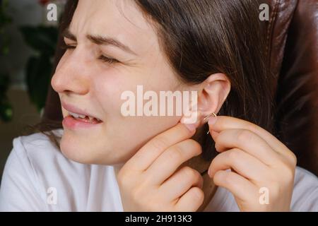 A woman tries to put an earring in her ear, earlobe problem, the hole is overgrown Stock Photo