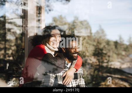Portrait of cheerful woman embracing boyfriend seen through window Stock Photo